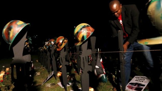 A volunteer arranges replicas of guns and helmets placed on the ground to symbolize Kenyan soldiers serving in the African Union Mission in Somalia (AMISOM) who were killed during an attack last week, at a memorial vigil within the 