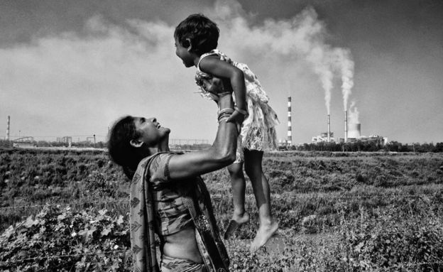 A woman carries a child with a thermal power plant in the background