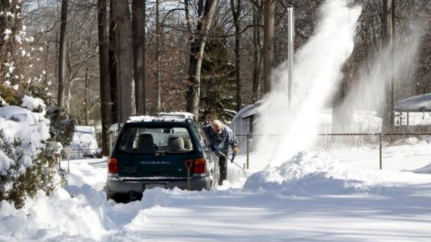 Frank Courtell clears snow with an electric snow blower on his driveway after a snowstorm inside the Washington DC