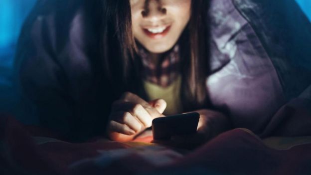 Una joven mira su teléfono en la oscuridad, en su cama