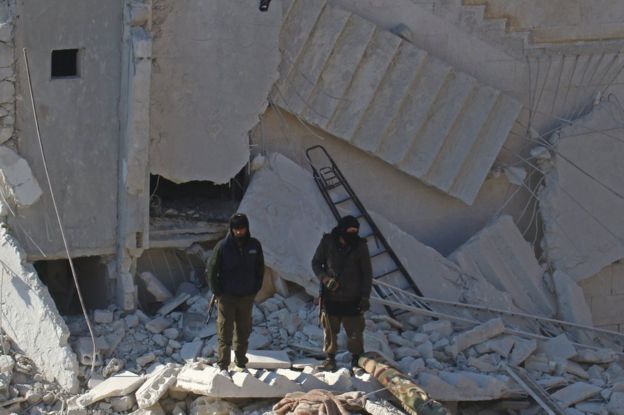 Rebel fighters stand next to building destroyed in air strike in rebel-held city of Idlib on 7 February 2017