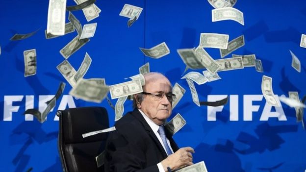 Fifa President Sepp Blatter at a press conference as fake dollar notes thrown by a British comedian fly around him (20 July 2015)