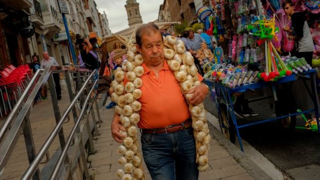 Un hombre con una ristra de ajos en una calle de España.