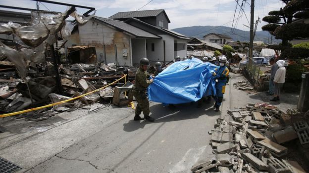 Rescue workers carry Yumiko Yamauchi, 93, on a stretcher covered in a blue plastic sheet, as they tread their way through broken tiles from a toppled house in Mashiki, Kumamoto prefecture, southern Japan (16 April 2016)