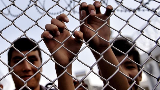 A migrant grabs a razor wire topped fence as the Greek prime minister visits a refugee and migrant registration camp in Mytilene, on the Greek island of Lesbos, on October 6, 2015.