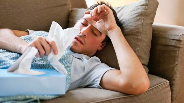 Un hombre tumbado en un sofá con una caja de toallas de papel