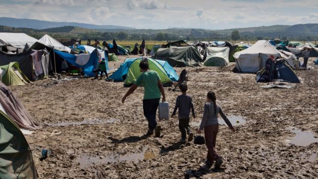 Migrants walk through mud at the migrant camp in Idomeni, Greece, Sunday 22 May 2016.