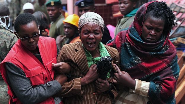 A crying woman flanked by two people who are linking arms with her and steering her somewhere