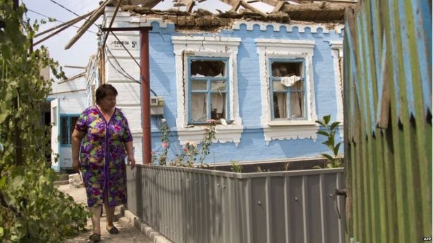 A resident walks in front of her house destroyed by shelling perpetrated by pro-Russian separatists in the village of Sartana, near Mariupol (17 August 2015)