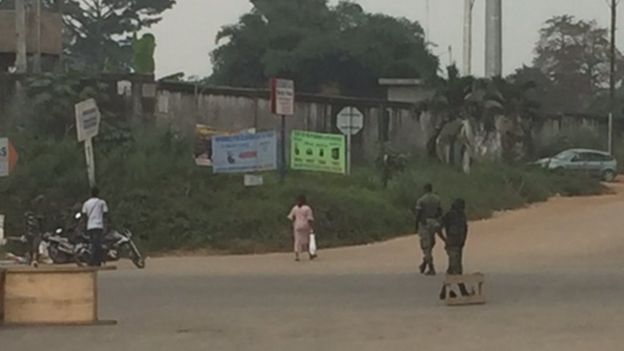 Quelques civils marchent dans la rue, devant les militaires mutins qui ont barré la route