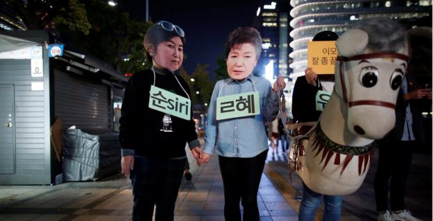 Protesters wearing masks of Choi Soon-sil (left) and President Park Geun-hye (centre), alongside someone dressed as a donkey, at a protest denouncing President Park on 27 October 2016 in Seoul.