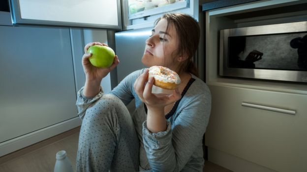 Mujer pensando en si comer una manzana o una dona