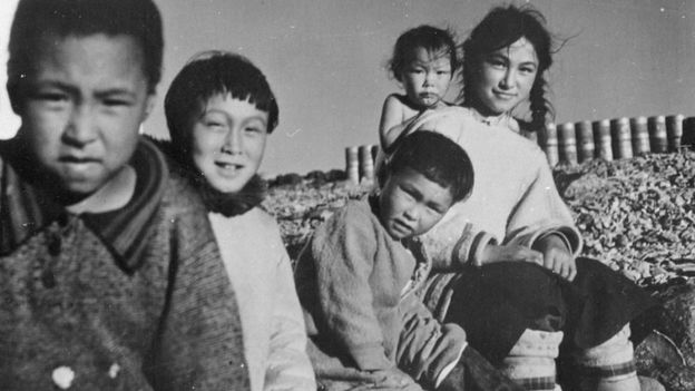 unknown boy, Johnny (Kavavow?) Lyall, Pat Napatchee Lyall, Bella Ningyooga Wilcox (née Lyall) carrying her baby sister Betty Novalinga Brewster (née Lyall), probably at Fort Ross, Nunavut, summer 1948.