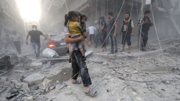 A Syrian man carries two girls covered with dust following a reported air strike by government forces on 9 July 2014 in the northern city of Aleppo.