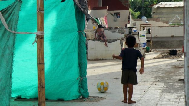 Un niño juega con una pelota de fútbol entre las casitas hechas de palos y plásticos.