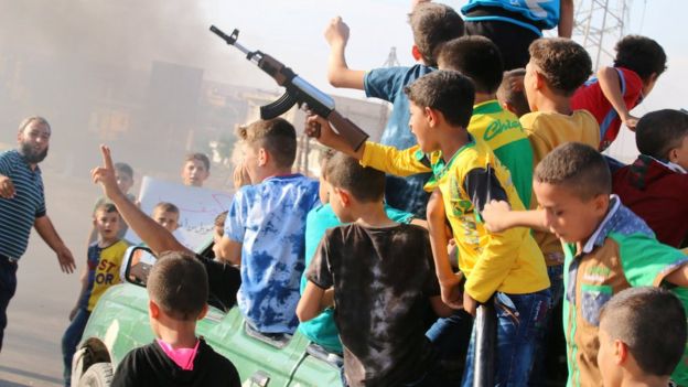 A boy carries a toy gun while riding a pick-up truck with other boys during a demonstration calling for aid to reach Aleppo near Castello road in Aleppo, Syria, September 14, 201