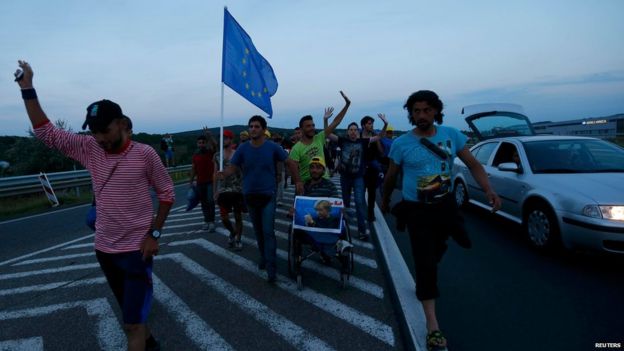 One of the migrants holds a portrait of German Chancellor Angela Merkel as they walk along the highway towards the border with Austria, out of Budapest, Hungary, September 4, 2015
