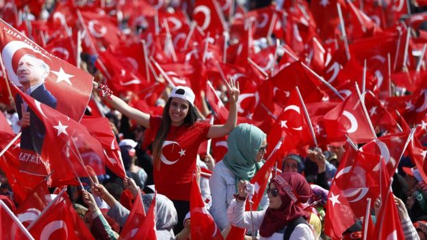 Kalabalık arasında genç bir kız elinde Türk bayrağı taşıyor.