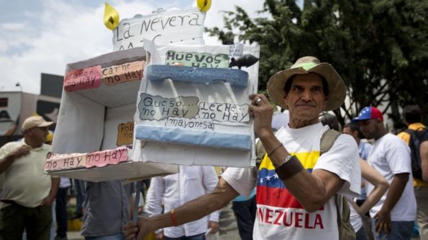 A man shows a cardboard box crafted to depict an empty refrigerator to indicate the shortage of products, during an opposition march in Caracas, Venezuela, Saturday, May 14, 2016.