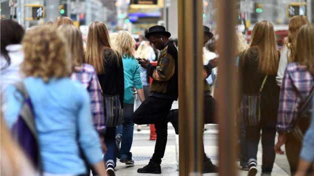 A man checks his cell phone as people walk past along a street in New York in 2014
