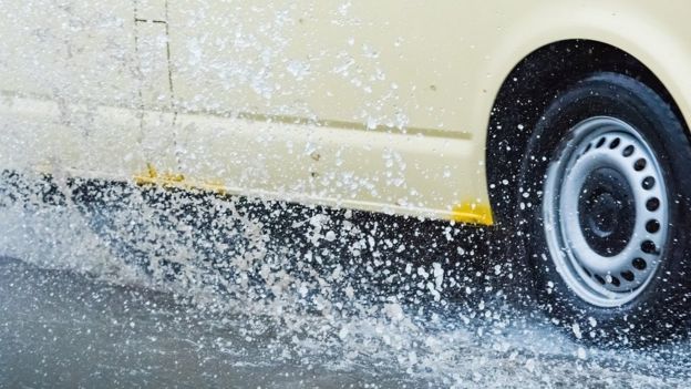 La rueda de un auto pasando por arriba de un charco de agua