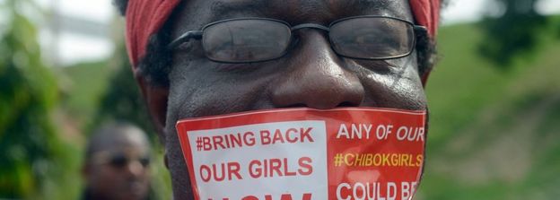 A man seals mouth with a branded sticker reading 'Bring Back Our Girls Now'