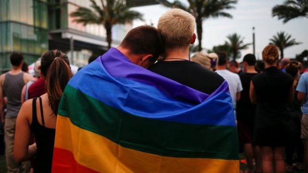 Men, draped in rainbow flag embrace ahead of candle light vigil in memory of victims of shooting at Pulse gay night club in Orlando, Florida. 13 June 2016