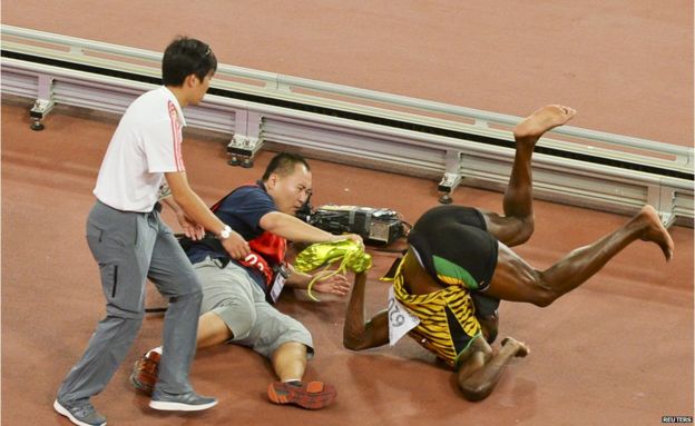 Usain Bolt of Jamaica (R) falls after being knocked over by a cameraman (C) on a Segway as he celebrates after winning the men's 200 metres final during the 15th IAAF World Championships at the National Stadium in Beijing, China, 27 August 2015