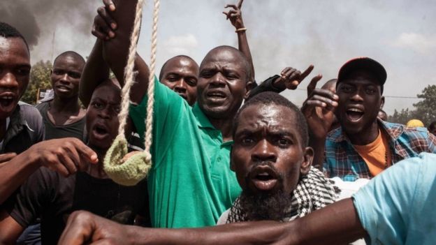 A Burkina Faso protestor holds a loaded slingshot as others gesture, in the city of Ouagadougou, Burkina Faso, Thursday, Sept. 17, 2015