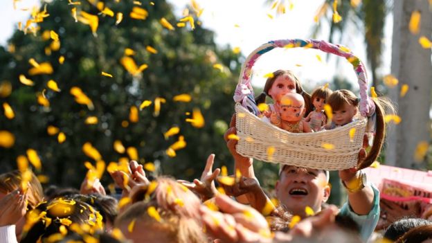 A man holds up a basket of the dolls at a religious event for them