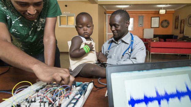 Baby using a pneumonia jacket with a technician, left and Brian Turyabagye, right