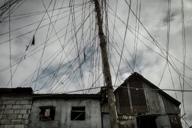 Un hombre asoma la cabeza de su pequeña ventana bajo las enredadas líneas eléctricas en el área de Parola, distrito de Tondo, Manila.