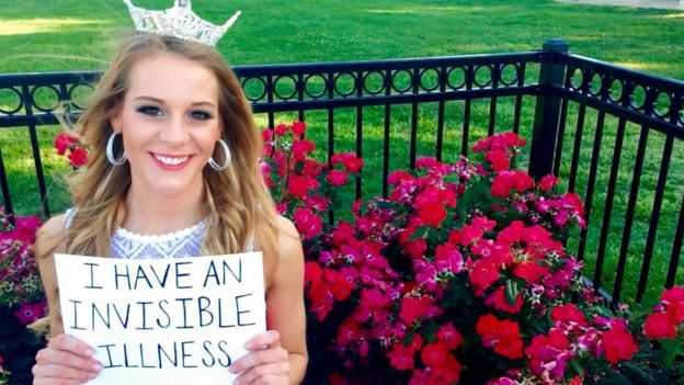 Victoria Graham holds a sign saying 'I have an invisible illness' in her pageant crown