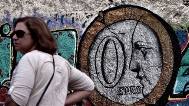 A woman stands in front of a graffiti bearing the number zero on a euro coin in central Athens on June 27, 2015