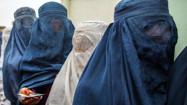 Afghan women wait to cast their ballot at a polling station dressed in blue and white burkas