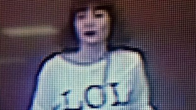 Grainy image shows a woman with brown hair wearing a T-shirt with the letters 