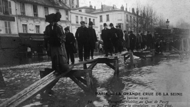 People balancing their way along a precarious-looking set of planks raised above the water