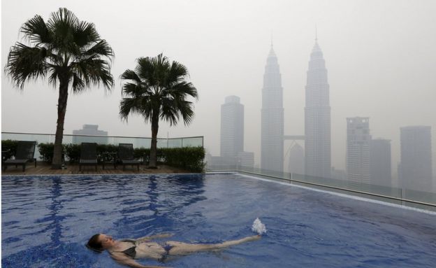 A woman swims in a rooftop pool in front of the Petronas Towers, shrouded by haze, in Kuala Lumpur