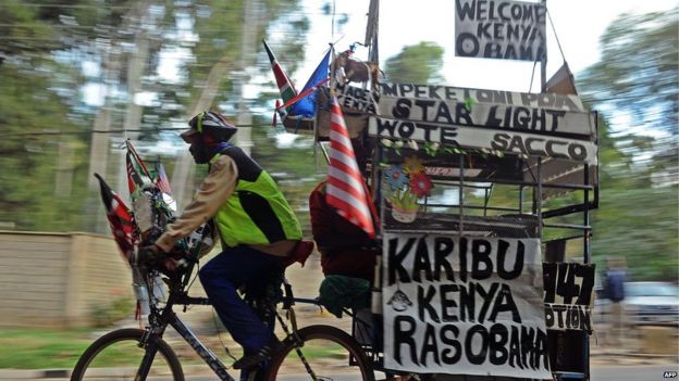 A man rides a bicycle and a trailer with messages reading 