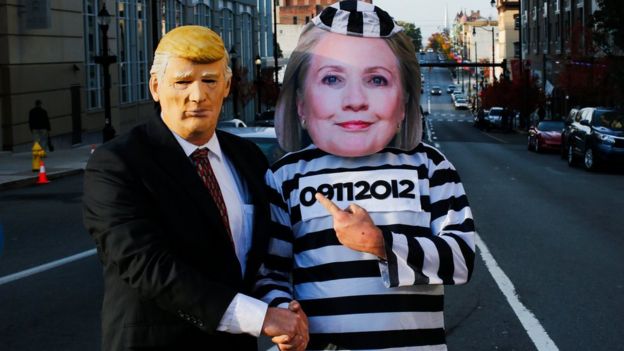 Dos personas disfrazadas de Trump de traje y de Hillary Clinton de presidiaria.