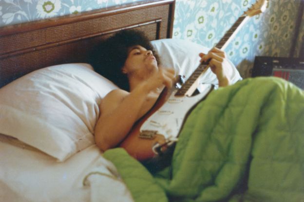 Prince plays a guitar in bed at his new home on France Avenue, April 1978