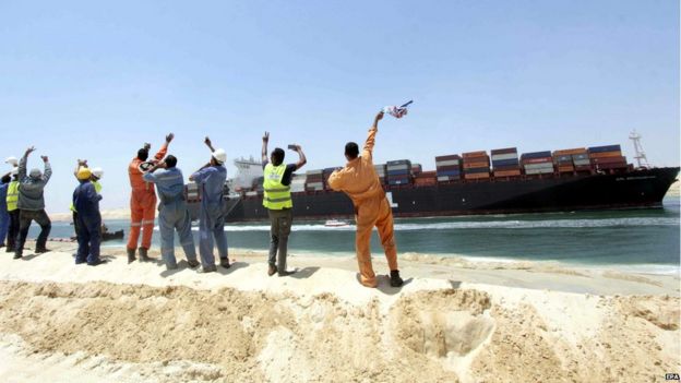 Egytpian workers wave towards a Container ship sailing on the waterway of the New Suez Canal on 25 July, 2015
