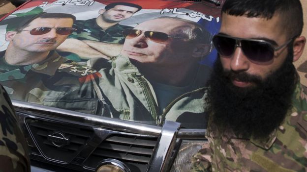 Syrian solder Hassan Muhammad stands near a car covered by a collage showing photos of faces of Russian President Vladimir Putin, right, Syrian President Bashar Assad, left, and a Syrian general, President's Assad brother, Maher Assad, centre, in Maarzaf, about 15 kilometres west of Hama, Syria, Wednesday, March 2, 2016