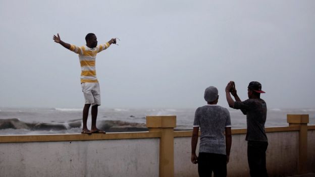 A man poses for a picture on a wall next to the sea ahead of Hurricane Matthew in Les Cayes, Haiti