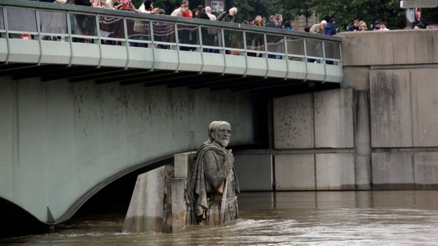 People looking at the floods stand on the Alma bridge by the Zouave statue which is used as a measuring instrument during floods in Paris, France Saturday June 4, 2016