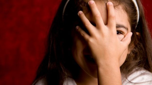 niña cubriendo su cara con la mano
