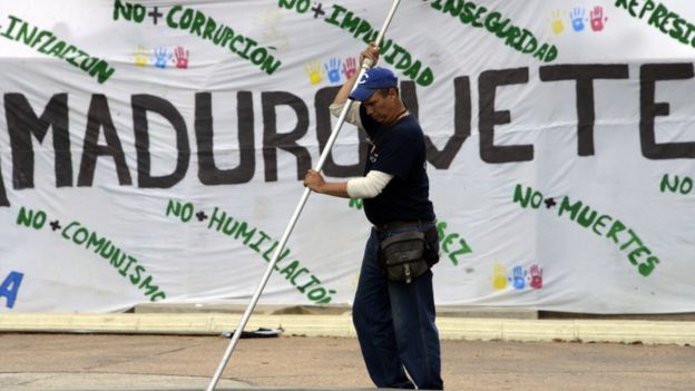Un trabajador frente a un cartel que pide la marcha de Maduro