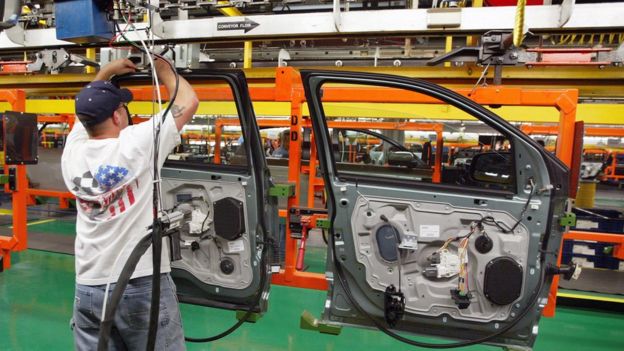 Hombre con una bandera de EE.UU. en la espalda trabajando en una fábrica de autos.