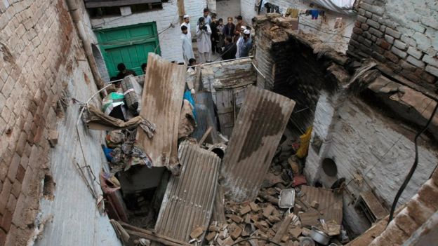 People stand outside a house damaged by an earthquake in Peshawar, Pakistan (26 Oct. 2015)