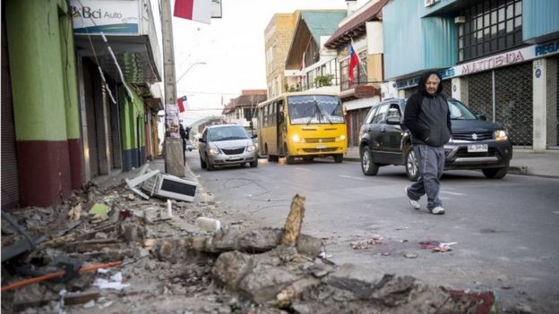 A man crosses a street next to rubble from a collapsed house after an earthquake in Illapel, some 200 km north of Santiago on 17 September, 2015.